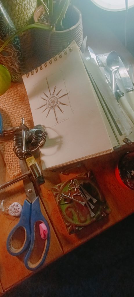 Open sketchbook with radial design on table surrounded by scissors and pliers