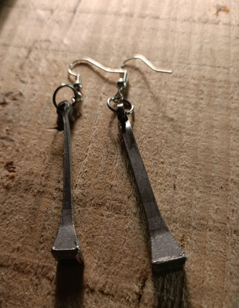 Horseshoe nail long earrings laying on a wooden block